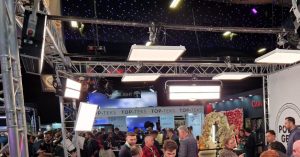 The lighting rig with GEMtiles and GEMflo products by Power Gems above the exhibition stands, with crowds of people attending a trade show
